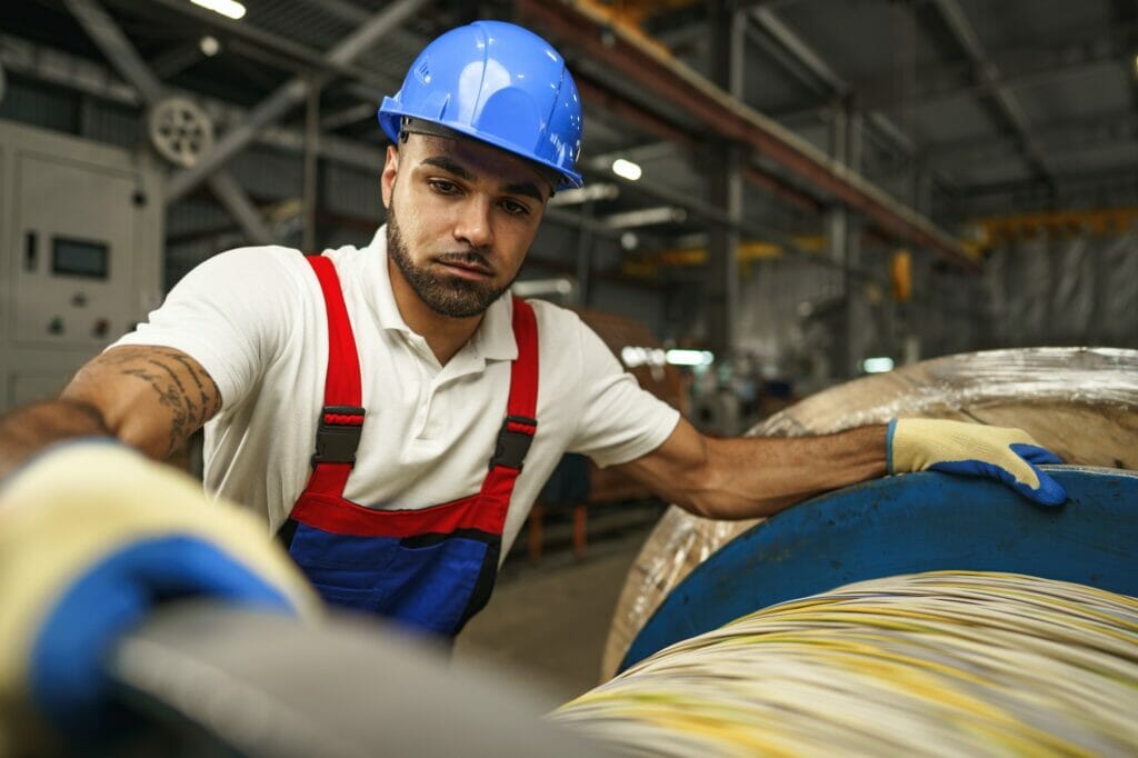 A young factory workman rolls heavy coil of electric cable