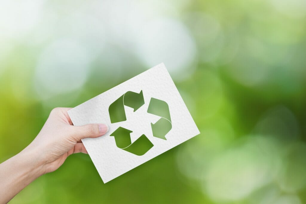 Environment concept. Hand holding white paper with recycle symbol on green bokeh background.